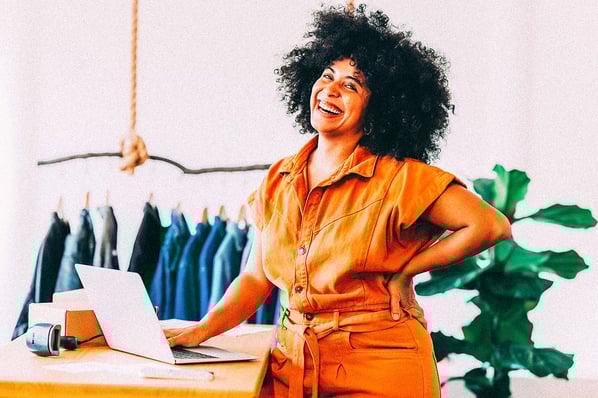Small business owner smiling in her retail shop while creating videos on her laptop